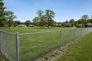 Long galvanized chain link fence running along a suburban property boundary on a clear day